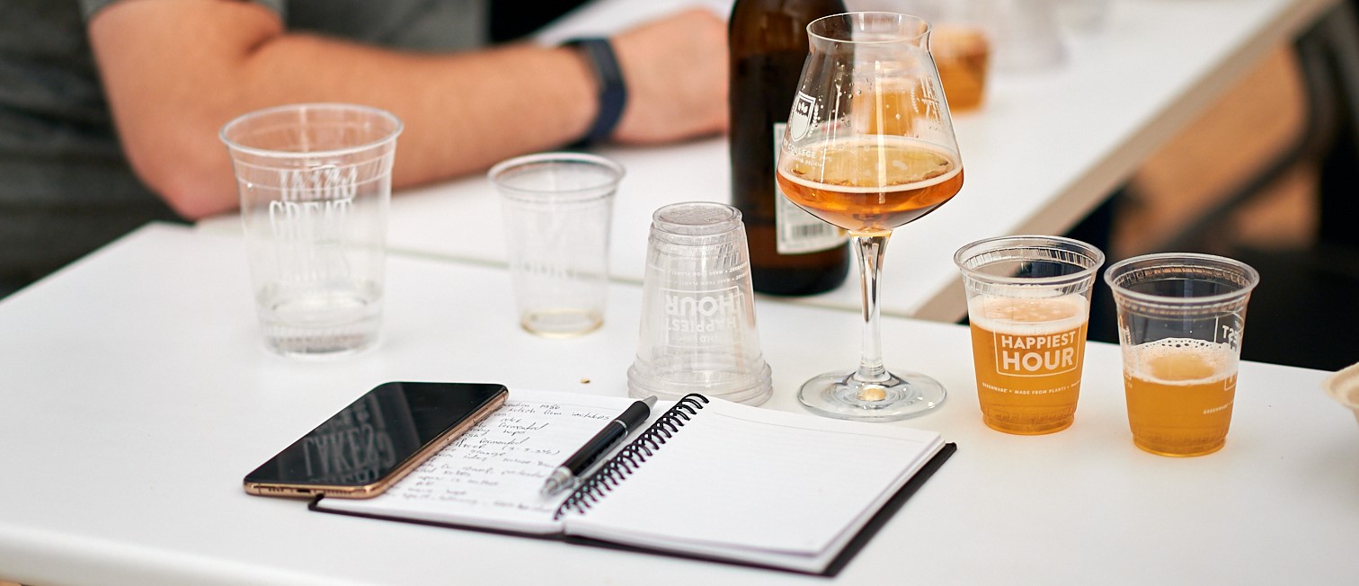 GLBC Hop College notebook and pen on a white desk with seated students and beer samples.