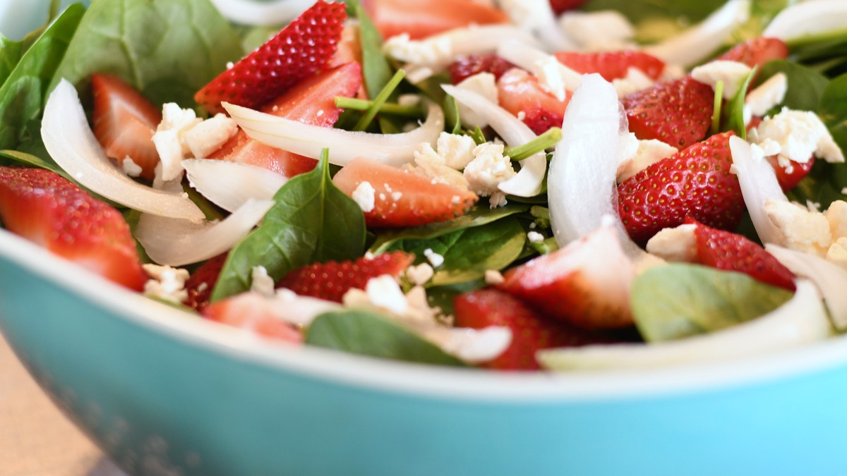 Blue bowl filled with strawberry spinach salad topped with onions and Strawberry Pineapple Wheat dressing