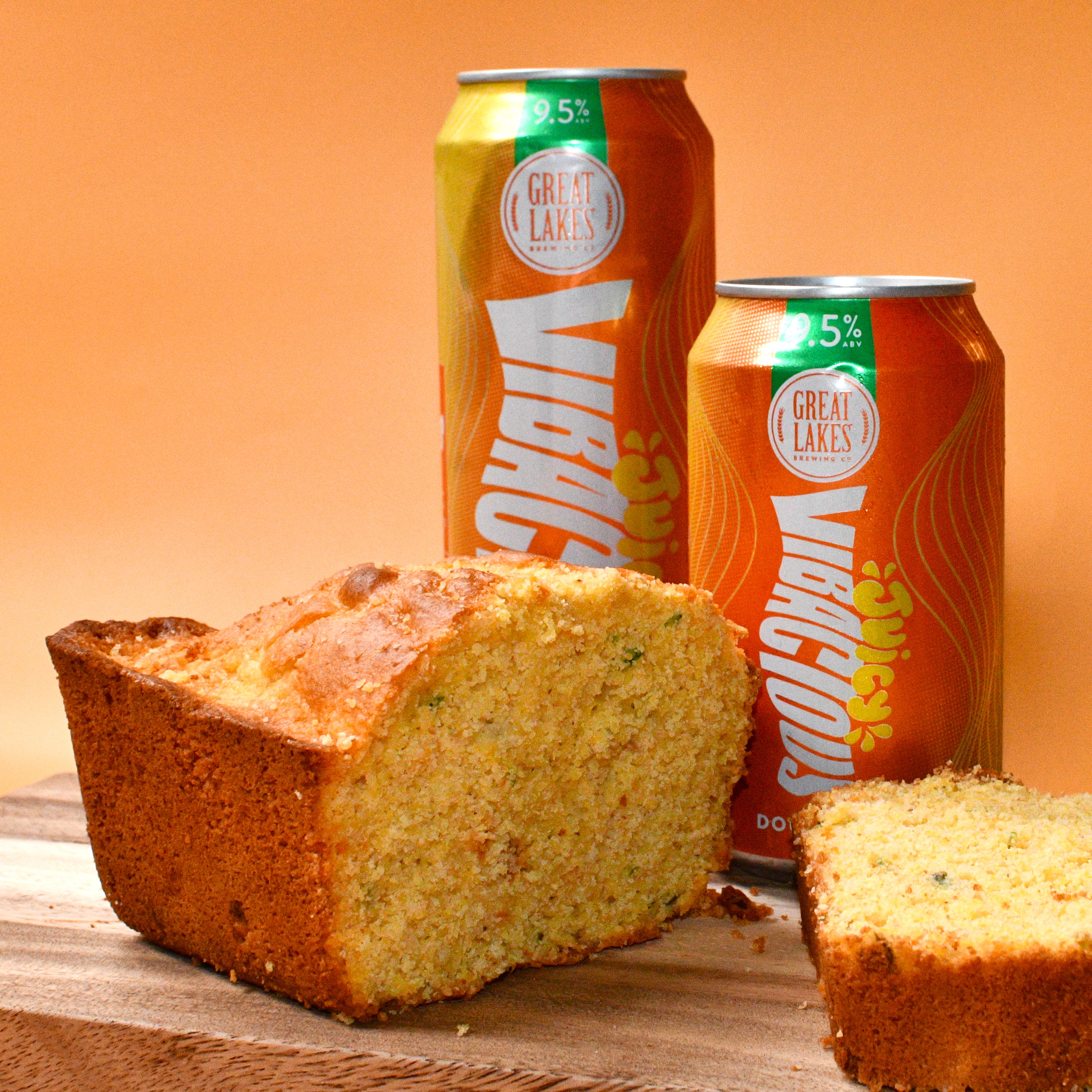 Half cornbread loaf with slice cut, in front of cans of Juicy Vibacious