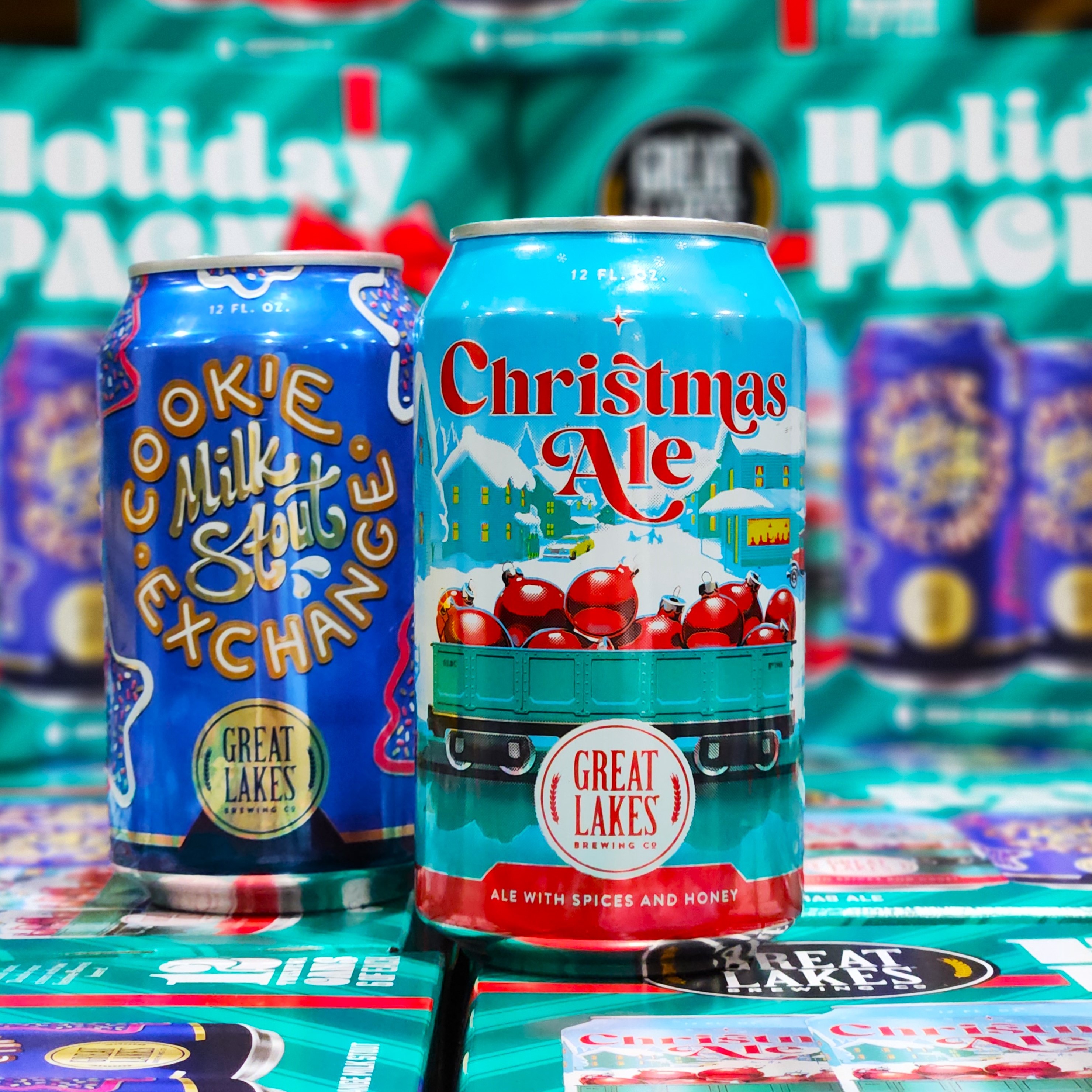 Cans of Cookie Exchange Milk Stout and Christmas Ale on a stack of Holiday Pack Variety Packs.