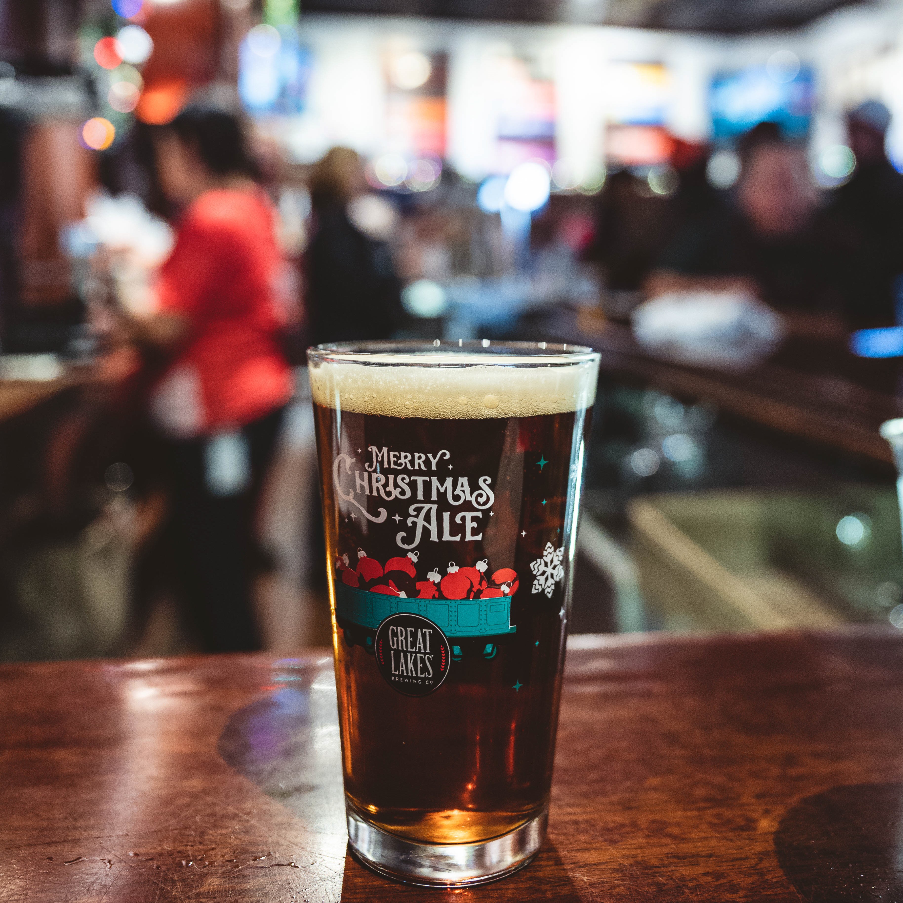 A pint of Christmas Ale in a glass printed with "Merry Christmas Ale" and the iconic train car on the brewpub bar.