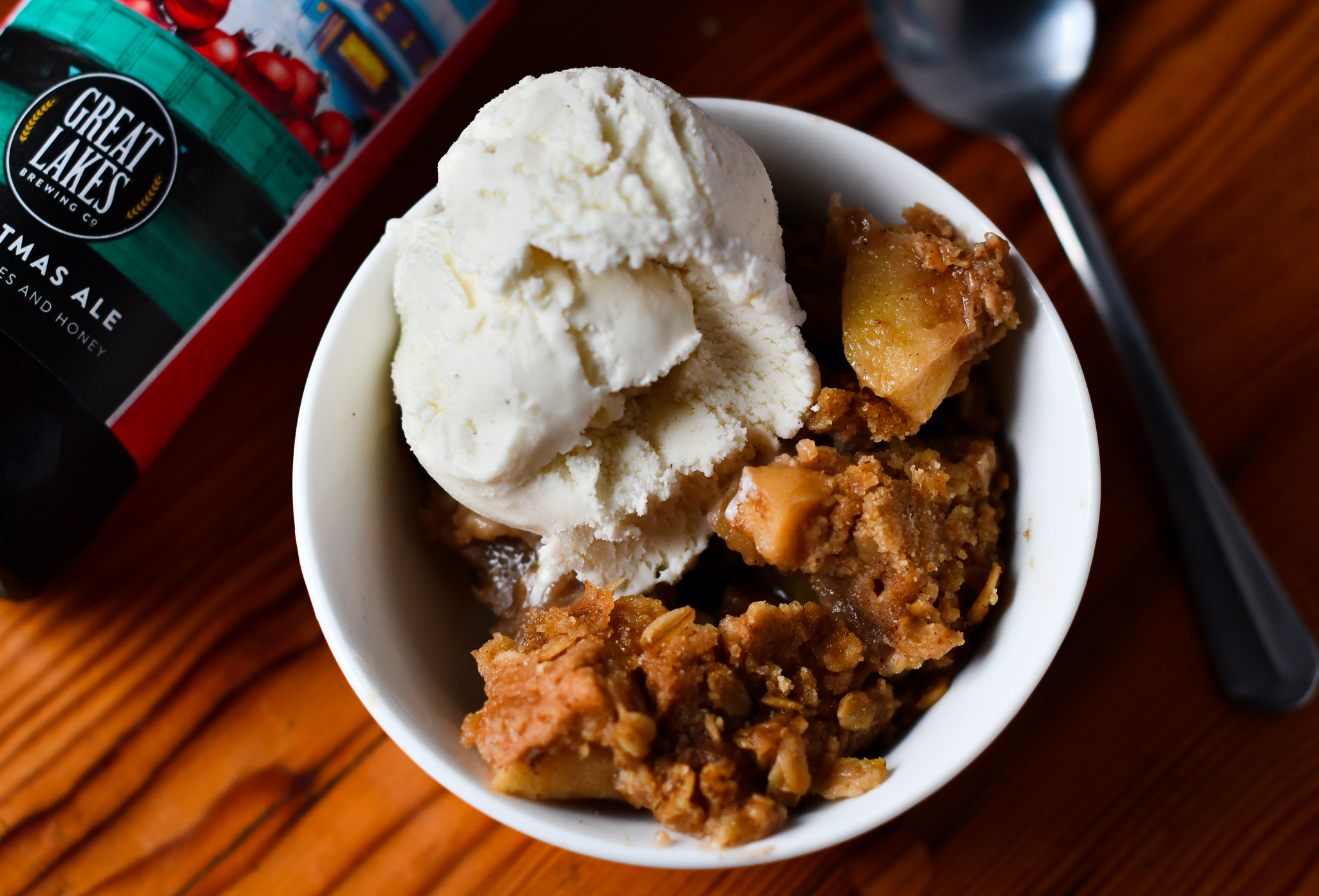 Apple crisp with ice cream scoop next to Christmas Ale bottle.