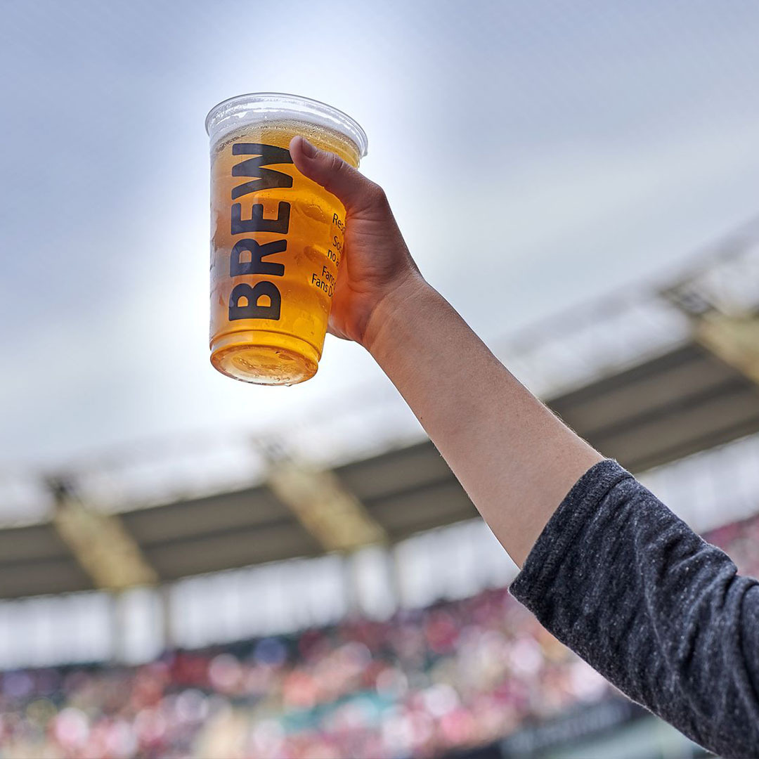 Hand holding a pour of draft beer at a baseball game.