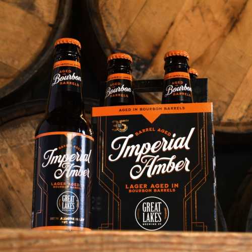 4 Pack and Bottle of Barrel Aged Imperial Amber Lager in front of wooden barrels