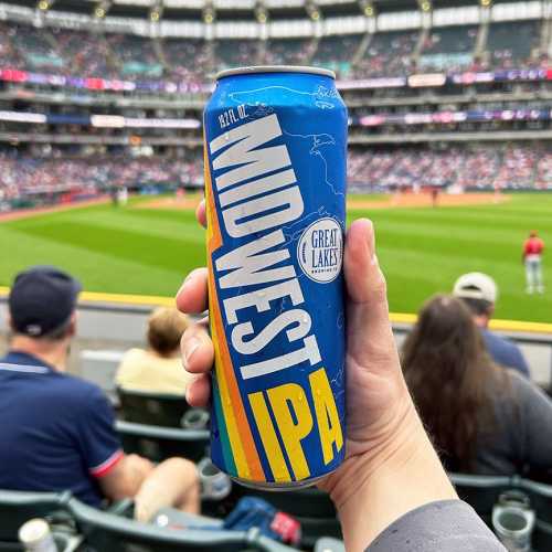 Hand holding a 19.2 oz. Can of Midwest IPA in front of a baseball field.