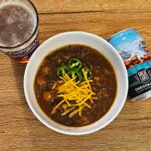 Bowl of Christmas Ale Short Rib Chili with can and pint of Christmas Ale